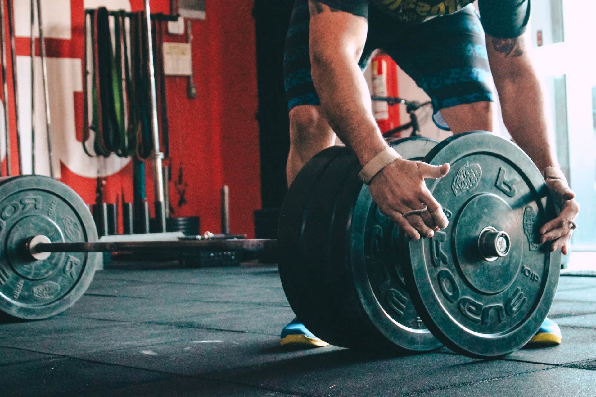 A guy in a gym putting 5 kilograms plates on a barbell